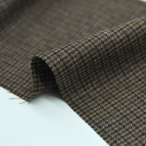 May include: Close-up of a folded piece of brown and black houndstooth fabric. The fabric has a classic pattern with small, repeating checks. The material appears to be a medium-weight woven textile, suitable for apparel or home decor projects.