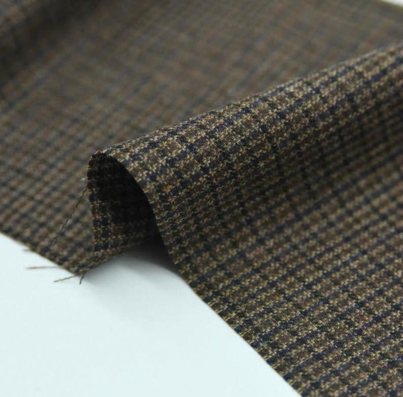 May include: Close-up of a folded piece of brown and black houndstooth fabric. The fabric has a classic pattern with small, repeating checks. The material appears to be a medium-weight woven textile, suitable for apparel or home decor projects.