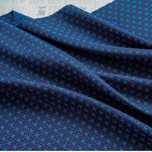 Pode incluir: Close-up de um tecido azul escuro com um padrão floral repetido em tons de azul-petróleo e marinho. O tecido é drapeado, mostrando a textura e o design. O padrão é um pequeno motivo floral simétrico.