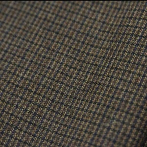 May include: Close-up of a brown and navy blue houndstooth fabric. The woven material has a repeating pattern of small squares, creating a textured appearance. The fabric is likely used for clothing or upholstery.