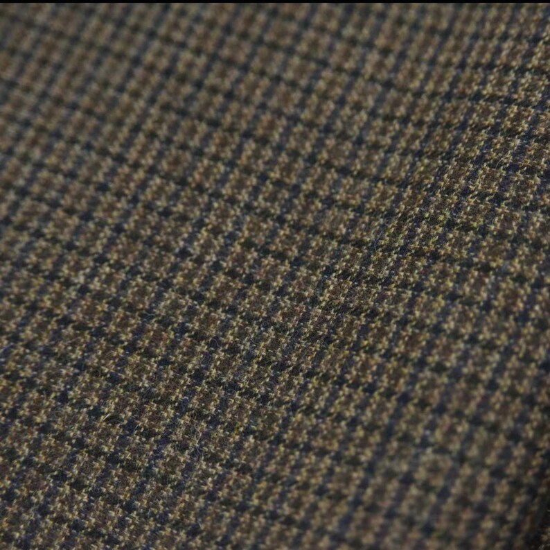 May include: Close-up of a brown and navy blue houndstooth fabric. The woven material has a repeating pattern of small squares, creating a textured appearance. The fabric is likely used for clothing or upholstery.