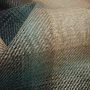 May include: Close-up of a folded fabric with a herringbone pattern. The fabric features a color gradient from teal to tan and brown. The texture is visible, with the weave creating a subtle diagonal effect.