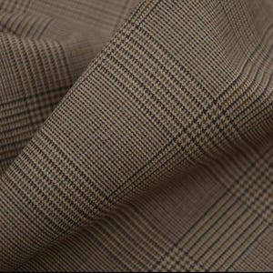 Op de afbeelding: Close-up van een gevouwen stof met een klassiek glen plaid patroon. De stof heeft een mix van bruine, beige en zwarte tinten, wat een textuur geeft. De diagonale vouwen geven diepte aan het textiel, geschikt voor kleding of stoffering.