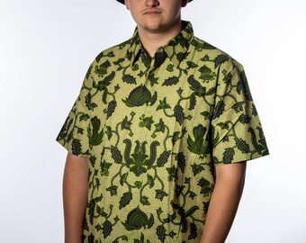 May include: A person wearing a black bucket hat and a short-sleeved button-down shirt. The shirt features a green and yellow floral pattern. The person is also wearing grey trousers.