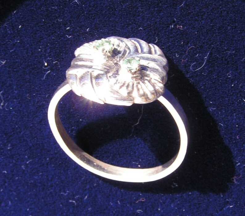 May include: A silver ring with a twisted design and two green gemstones set in the top.