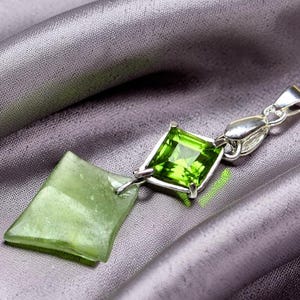 Puede incluir: Un colgante de plata con una piedra preciosa de color verde lima de corte cuadrado conectada a una piedra más grande, irregular y translúcida de color verde pálido. El engaste es de plata pulida e incluye una anilla de plata.