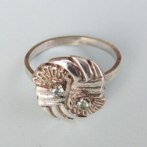 May include: A silver ring with a knot design and two green gemstones.