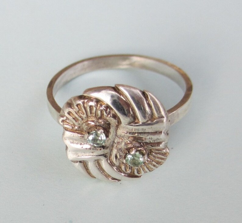 May include: A silver ring with a knot design and two green gemstones.