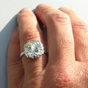 May include: A silver ring with a woven design and two green gemstones.