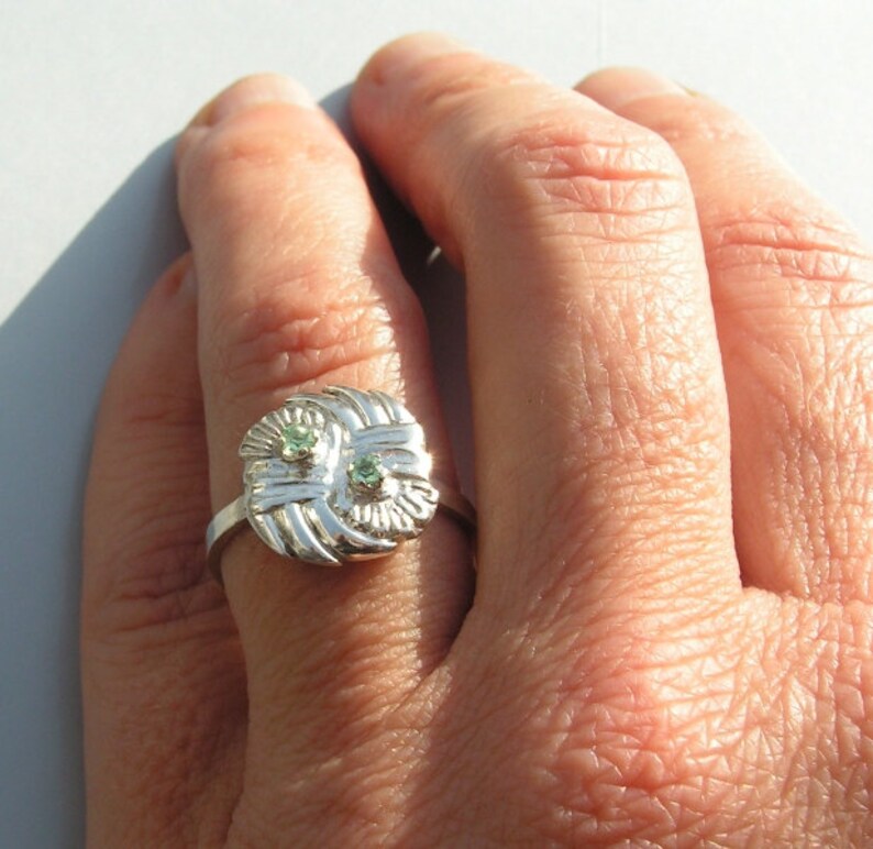 May include: A silver ring with a woven design and two green gemstones.