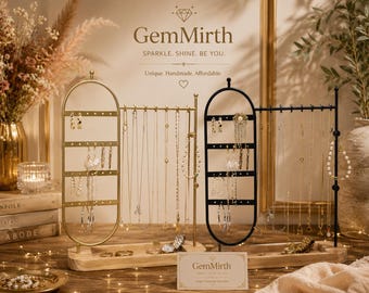 May include: Two jewelry stands with oval frames and horizontal bars for hanging necklaces and earrings. One stand is gold-toned metal, the other is black metal. Both feature light-colored wooden bases with small trays for rings and accessories.