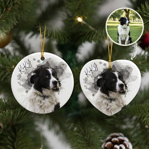 May include: Two white ceramic dog ornaments, one round and one heart-shaped, hang from gold strings. Each features a black and white dog portrait with the name "Kiky" and a watercolor-style gray background. A small photo of the dog is in the background.