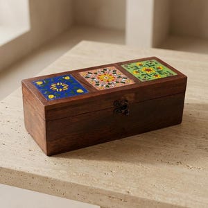 May include: A rectangular dark brown wooden box featuring three square decorative inlays on the lid. The inlays display floral patterns in blue, pink, and green with yellow accents. A small metal latch is centered on the front of the box.