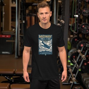 Pode incluir: Uma t-shirt preta de manga curta com uma impressão gráfica de um avião militar sobrevoando um navio. O texto diz MIDWAY, JUNE 4-7 1942, THE TURNING POINT OF THE PACIFIC, com um pequeno emblema de estrela na base do design retangular.