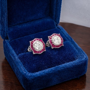 Peut inclure: Une paire de boucles d'oreilles à clous avec un diamant central taille brillant ronde entouré d'un halo de rubis taille baguette trapézoïdale, montés sur une monture en métal argenté à bord festonné, présentés dans un écrin en velours bleu.