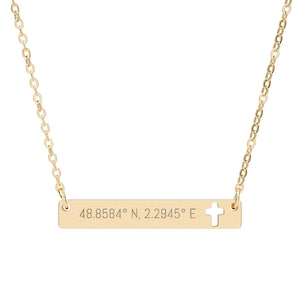 May include: A gold-colored necklace with a delicate chain. The pendant is a rectangular bar with the coordinates "48.8584° N, 2.2945° E" engraved on it, and a cross cutout on the right side.