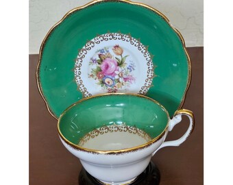 May include: A vintage teacup and saucer set with a green and gold floral design. The cup and saucer are both trimmed with a gold band and feature a delicate floral pattern in the center.