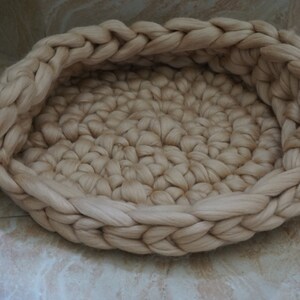 May include: A cream-colored woven pet bed made of thick yarn. The bed is round and has a raised edge.