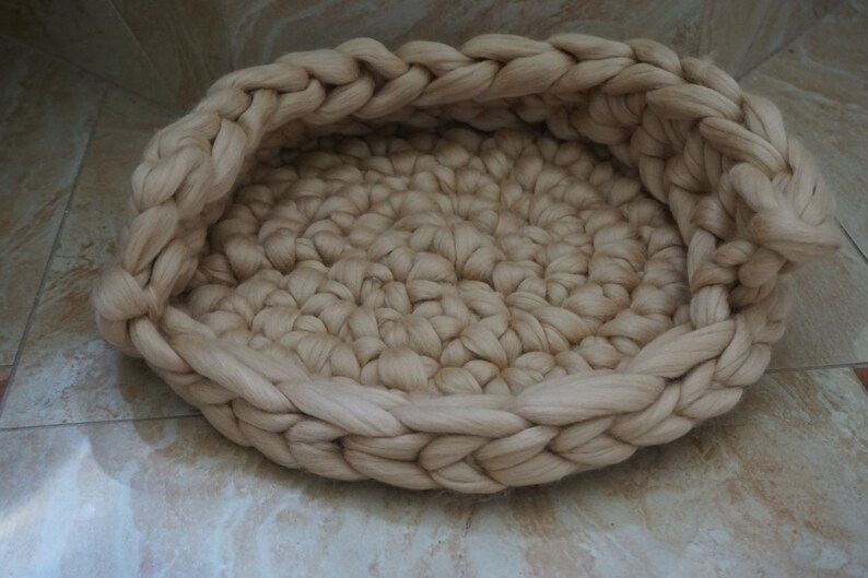 May include: A cream-colored woven pet bed made of thick yarn. The bed is round and has a raised edge.