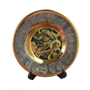 May include: A circular decorative plate featuring a central green medallion with a gold dragon illustration. The border has a marbled gray and white pattern with a gold rim. A gold label at the bottom reads 24KT GOLD.