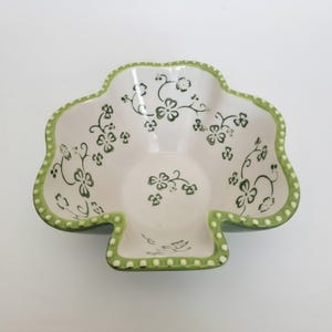 May include: A clover-shaped ceramic bowl with a white interior and a green dotted rim. The bowl features a delicate green floral pattern of small leaves and vines scattered across the interior surface, creating a cohesive and detailed design.