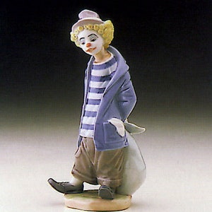 May include: A porcelain figurine of a clown with a blue and white striped shirt, a blue jacket, and a white hat. The clown is holding a white bag and is standing on a small base.