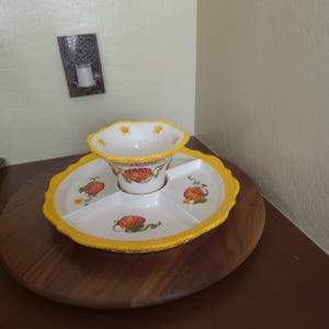 May include: A white ceramic serving platter with three divided sections and a central bowl, featuring a yellow rope-textured rim and painted orange pumpkin motifs with green vines and small yellow flowers on the interior surfaces.