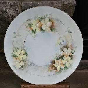 May include: A white porcelain plate with a gold rim and a delicate floral design featuring yellow flowers and green leaves.