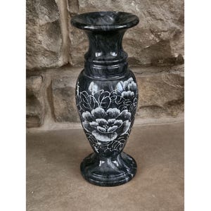 May include: A black marble vase with a white floral design. The vase has a wide mouth and a narrow base.