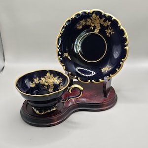 May include: A white ceramic mug with a black handle and the text "But First, Coffee" in a bold, black font. The mug is filled with a dark liquid, likely coffee, and rests on a light-coloured surface.