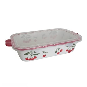 May include: A rectangular white ceramic baking dish with a cherry pattern featuring red fruit and green leaves. The dish includes a clear plastic lid with a scalloped red rim decorated with white polka dots and integrated side handles.