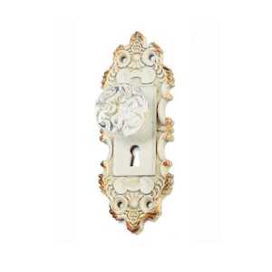 May include: White ornate door knob with a clear glass knob and a keyhole. The door knob has a distressed finish.