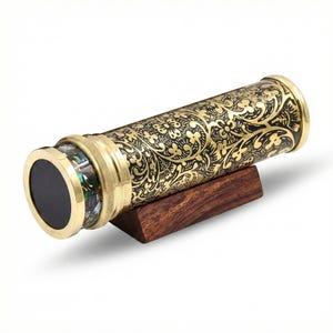May include: A brass kaleidoscope with a black and gold floral pattern. The kaleidoscope rests on a small, dark wooden stand. The end of the kaleidoscope features a black circle and iridescent accents.