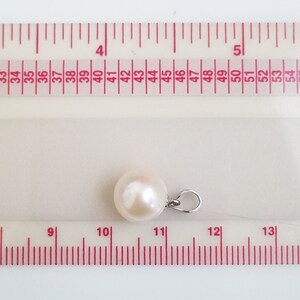 May include: A white pearl pendant with a silver bail, measured against a ruler. The pearl is approximately 11 mm in diameter.