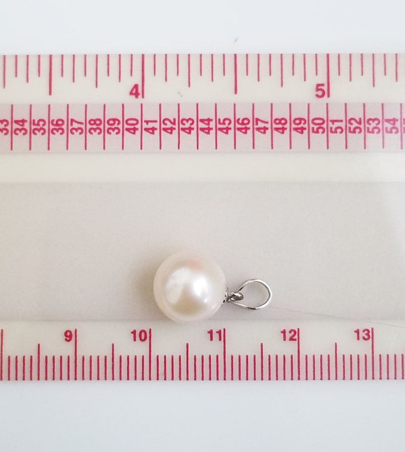 May include: A white pearl pendant with a silver bail, measured against a ruler. The pearl is approximately 11 mm in diameter.