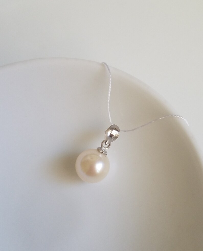 May include: A white pearl pendant on a silver chain. The pearl is round and smooth, and the chain is delicate.