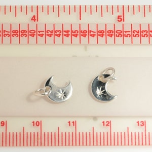 May include: Two silver crescent moon charms with a star design. The charms are approximately 3.2 cm in length and are shown against a white background with a ruler for scale.