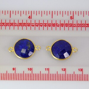 Pode incluir: Dois pingentes redondos de conex&atilde;o dourados com uma pedra preciosa de l&aacute;pis-laz&uacute;li azul escuro no centro. Os pingentes medem aproximadamente 2,5 cm de di&acirc;metro e t&ecirc;m um la&ccedil;o de cada lado para prender em joias.