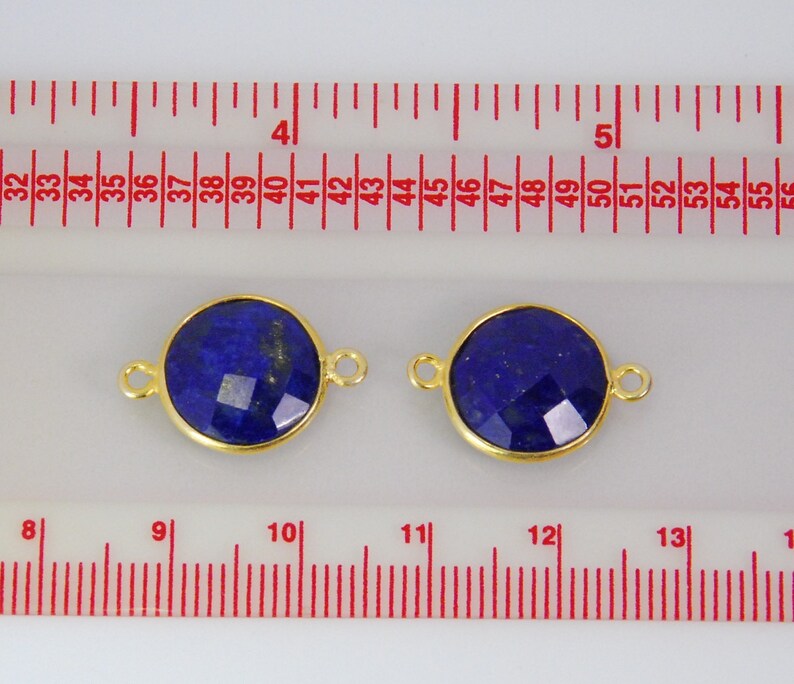 Pode incluir: Dois pingentes redondos de conex&atilde;o dourados com uma pedra preciosa de l&aacute;pis-laz&uacute;li azul escuro no centro. Os pingentes medem aproximadamente 2,5 cm de di&acirc;metro e t&ecirc;m um la&ccedil;o de cada lado para prender em joias.