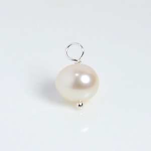 May include: A white pearl pendant with a silver loop and a small silver bead at the bottom.