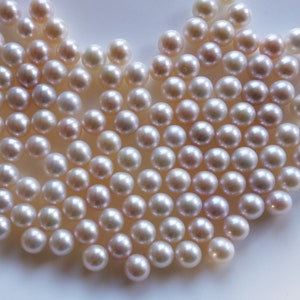 May include: A close-up of a large group of white pearls, arranged in a heart shape. The pearls are smooth and lustrous, with a slight iridescent sheen.