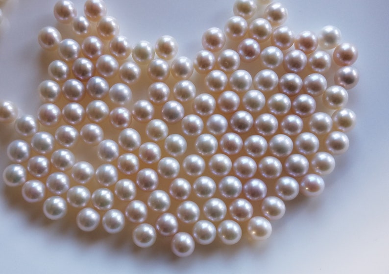 May include: A close-up of a large group of white pearls, arranged in a heart shape. The pearls are smooth and lustrous, with a slight iridescent sheen.