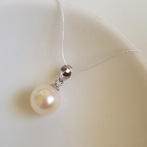 May include: A white pearl pendant on a silver chain. The pearl is round and smooth, and the chain is delicate.