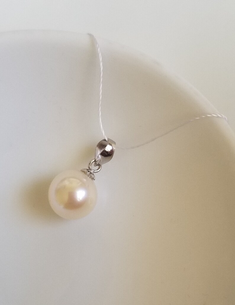 May include: A white pearl pendant on a silver chain. The pearl is round and smooth, and the chain is delicate.