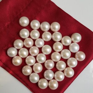 May include: A collection of white pearls in various sizes, displayed on a red velvet pouch. The pearls are smooth and lustrous, with a subtle iridescent sheen.