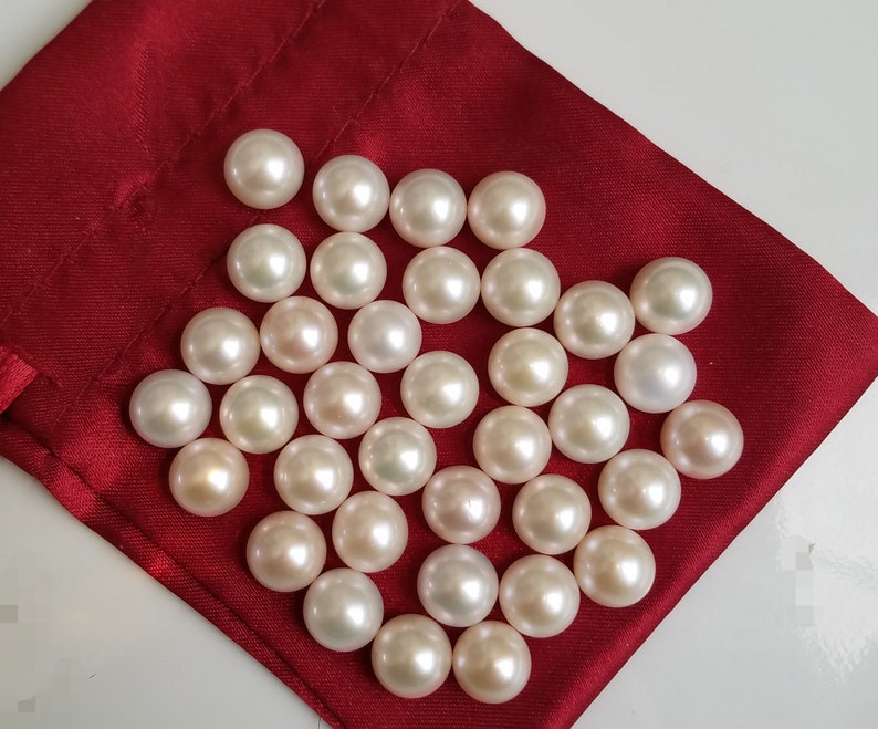 May include: A collection of white pearls in various sizes, displayed on a red velvet pouch. The pearls are smooth and lustrous, with a subtle iridescent sheen.
