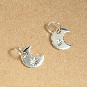 May include: Two silver crescent moon charms with a star design. The charms have a loop at the top for attaching to a necklace or bracelet.