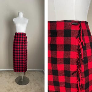 May include: A red and black plaid wrap skirt with a fringe detail. The skirt is made of a thick, woven fabric and has a high waist.