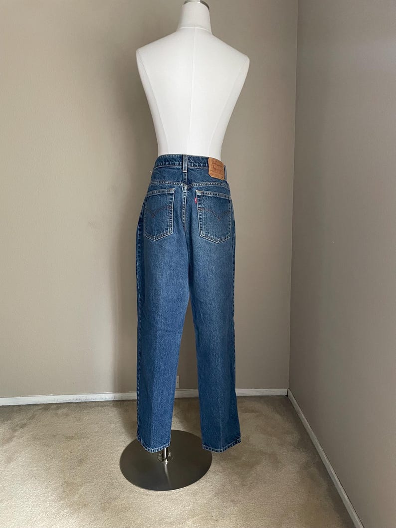 Peut inclure: Un jean bleu denim avec un patch en cuir marron au dos. Le jean est sur un mannequin et a une coupe droite.