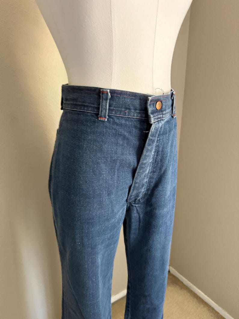 K&ouml;nnte beinhalten: Blaue Jeans aus Denim mit hoher Taille und Knopfverschluss. Die Jeans haben ein klassisches F&uuml;nf-Taschen-Design und ein gerades Bein. Der Denim hat ein leicht verwaschenes Aussehen.